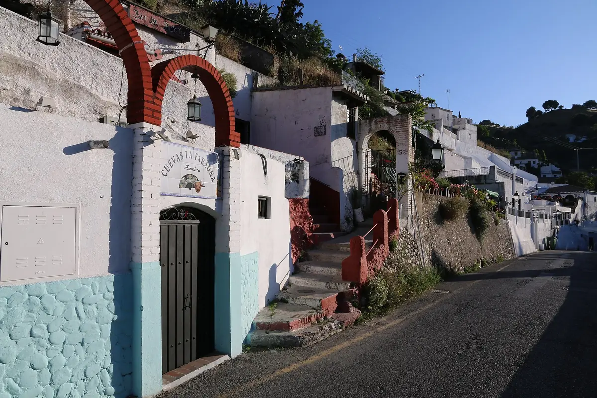 Whitewashed cave houses with red brick arches and a stepped path beside a road on a Sacromonte hillside
